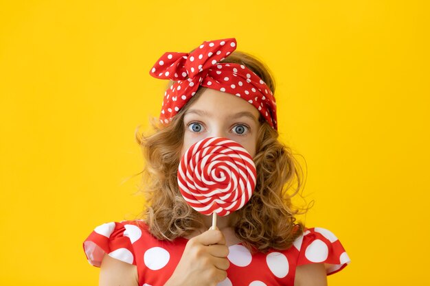 Verrast tienermeisje met rode lolly tegen gele muur