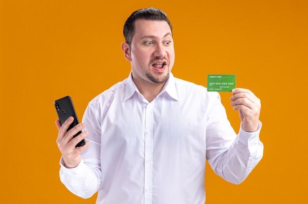 Verrast volwassen Slavische zakenman die telefoon vasthoudt en naar creditcard kijkt