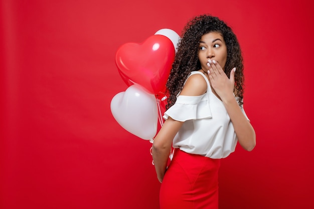 Verrast zwarte vrouw met kleurrijke ballonnen geïsoleerd op rood