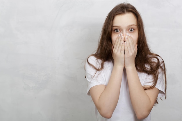 Verraste jonge vrouw die een wit t-shirt draagt dat tegen een lichte achtergrond wordt geïsoleerd