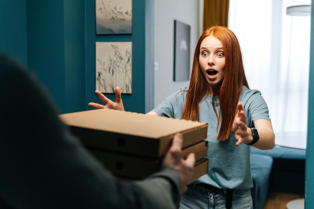 Verraste jonge vrouw die papieren dozen met hete pizza ontvangt van een onherkenbaar koeriersmannetje in de deuropening thuis