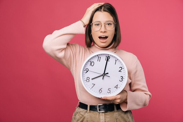 Verraste jonge vrouw houdt hand op het hoofd en een witte ronde klok