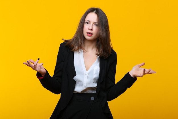 Verraste jonge vrouw in een pak op een gele achtergrond Emotioneel portret van een zakenvrouw