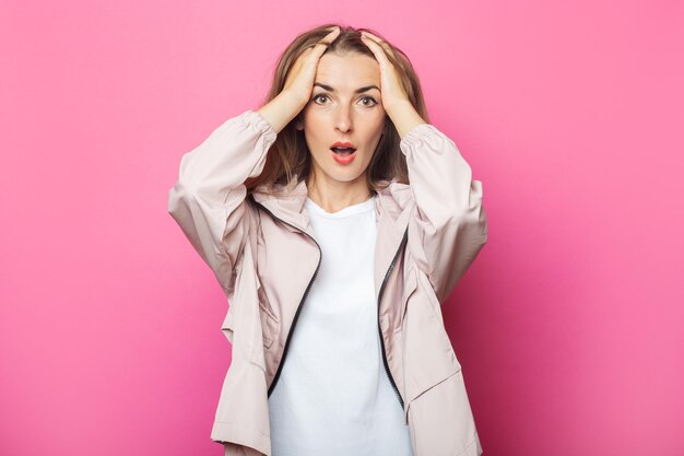 Verraste jonge vrouw in roze jasje, roze geïsoleerde achtergrond.