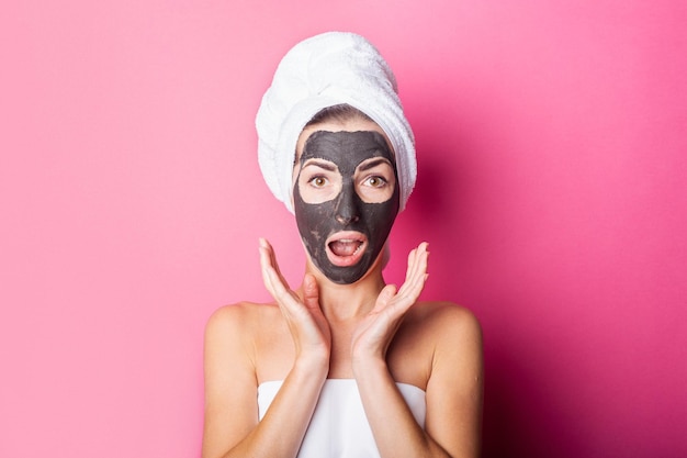 Verraste jonge vrouw met zwart masker op haar gezicht met een handdoek op haar hoofd op een roze achtergrond