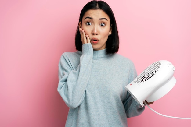 Verraste vrouw die in warme kleren radiator op roze achtergrond houdt