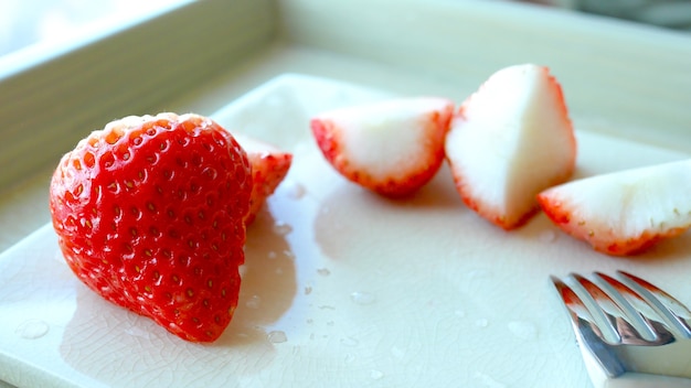 Vers aardbei en stuk fruit op witte plaat.