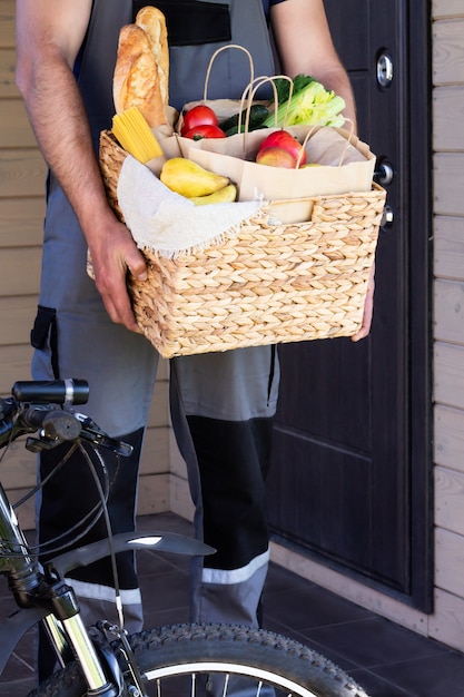 Foto vers biologisch brood, groenten, groenten en fruit, granen en pasta in een rieten mand in de handen van een fietskoerier. fiets milieuvriendelijke levering of schenking van ecologisch boerderijvoedselconcept.