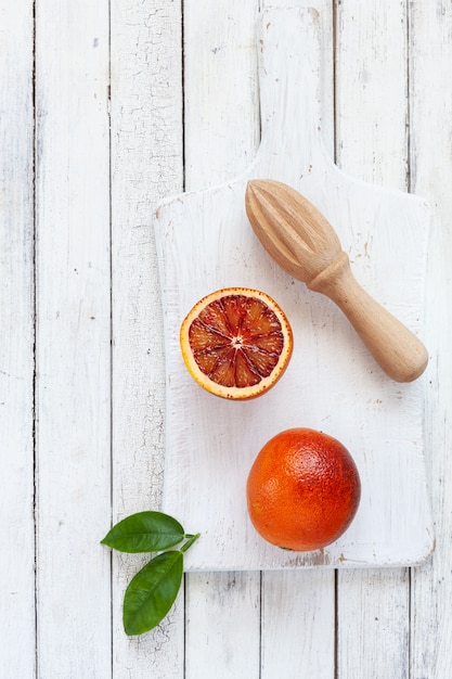 Vers bloed oranje vruchten met houten juicer op witte houten achtergrond