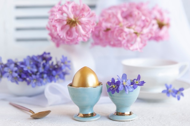 Vers boeket van delicate lentebloemen levermos Hepatica Nobilis en een gouden ei in een eierkraam