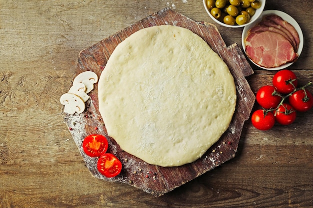 Vers deeg bereid voor pizza met tomaten en gesneden champignons op een houten plank close-up
