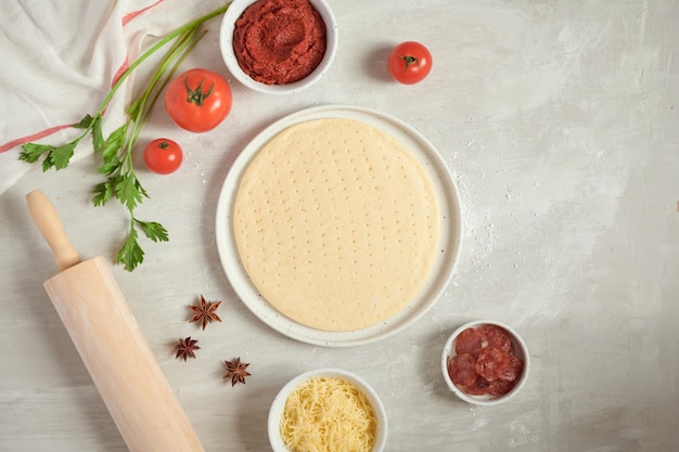 Vers deeg pizzabodem en ingrediënten op een witte tafel bovenaanzicht