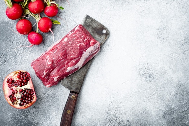 Vers en rauw rundvlees. Hele stuk ossenhaas met steaks en kruiden klaar om te koken set, op oude slagers hakmes, op grijze stenen achtergrond, bovenaanzicht plat lag, met kopie ruimte voor tekst