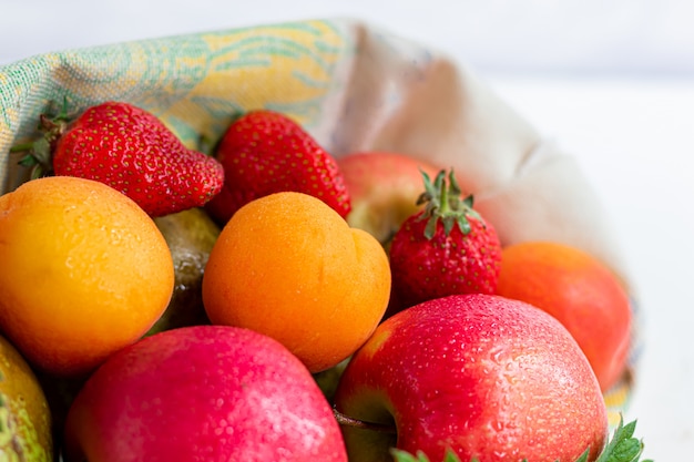 Foto vers fruit in een eco katoenen tas op een tafel in de keuken. met appels en peren, abrikozen en aardbeien, handelsconcept zonder afval. verbied plastic.