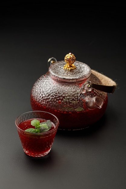 Vers fruit thee in glazen beker met theepot op achtergrond