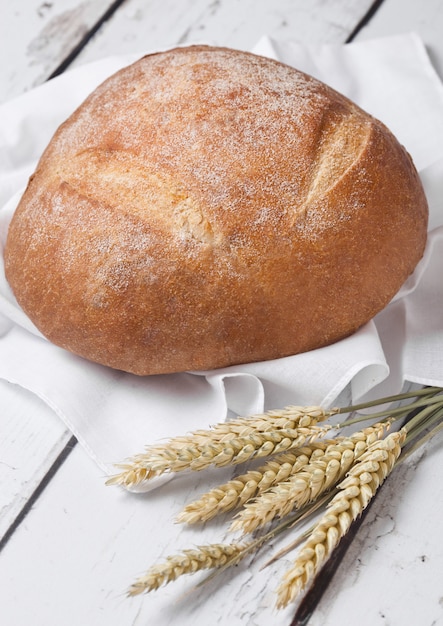 Vers gebakken brood met keukenhanddoek en tarwe op witte houten bord