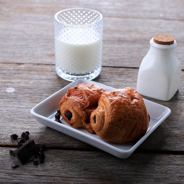 Vers gebakken chocoladecroissants (Pain au Chocolat) met melk voor het ontbijt. Geserveerd op witte plaat op rustieke tafel Kopieer ruimte voor tekst