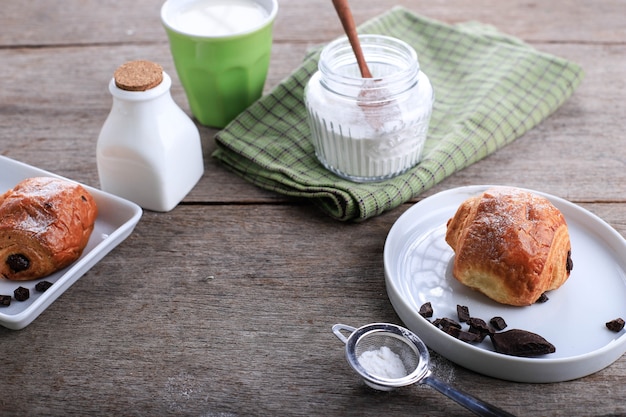 Vers gebakken chocoladecroissants (Pain au Chocolat) met melk voor het ontbijt. Geserveerd op witte plaat op rustieke tafel Kopieer ruimte voor tekst