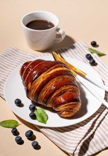 Vers gebakken croissant met chocolade op een wit bord en bosbessen op een gele achtergrond met een kop zwarte koffie Het concept van een heerlijk zelfgemaakt ontbijt