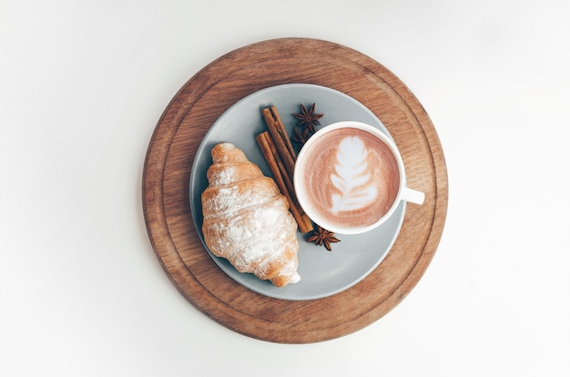 Vers gebakken croissant met koffiekopje en latte art, kaneel