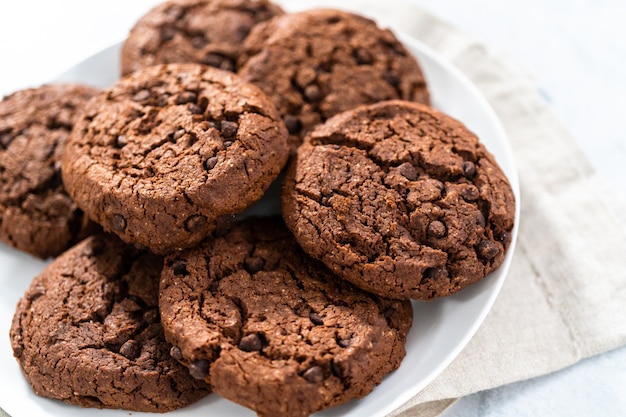 Vers gebakken dubbele chocoladeschilferkoekjes op een witte plaat.