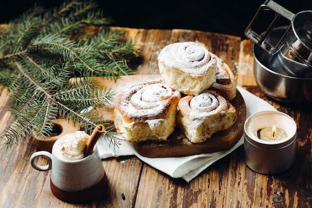 Vers gebakken kerst broodjes met poeder en een warme chocolademelk met kaneelstokje over rustieke feestelijke tafel.