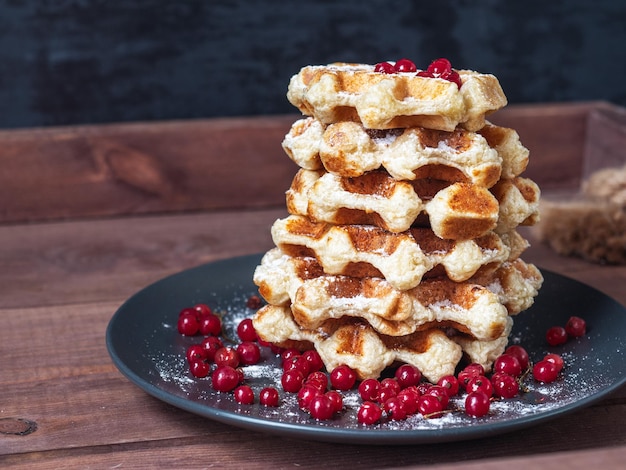 Foto vers gebakken weense wafels met suikerpoeder en bessen op een zwarte bord op een houten dienblad