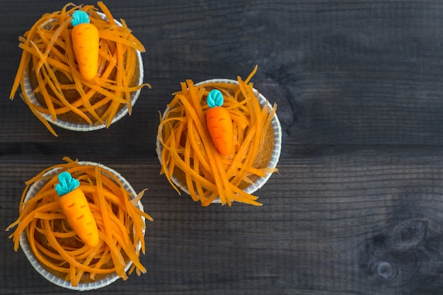 Vers gebakken wortelmuffins die met verse wortelspaanders en marsepeinwortelen op houten achtergrond worden verfraaid. Nationale Carrot Cake Day.