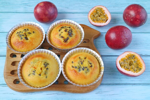 Vers gebakken zelfgemaakte passievruchten muffins in mallen op broodplank met vers fruit verspreid over lichtblauwe tafel