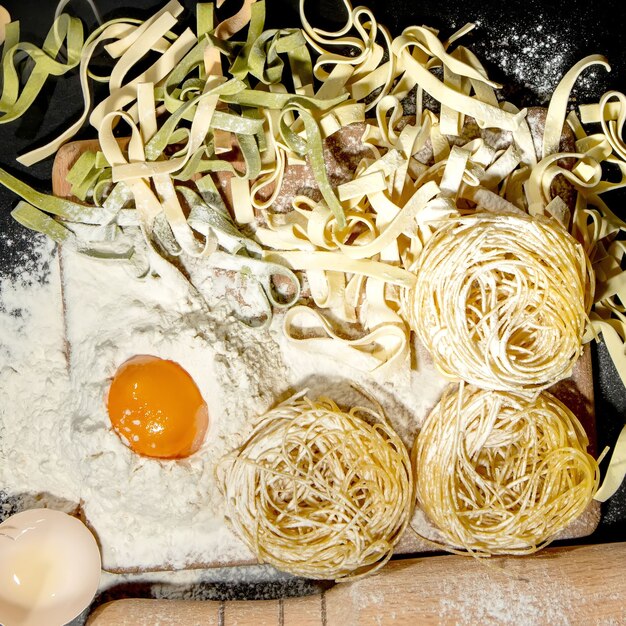 Vers gekookte pasta ligt op een donker oppervlak bestrooid met bloem. Italiaanse pasta. Tagliatelle. Rauwe pasta. Italiaans pastarecept. Bovenaanzicht, kopieer ruimte.