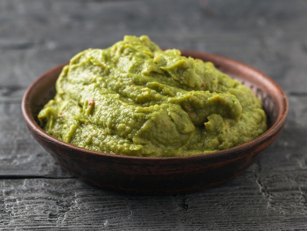 Vers gemaakte guacamole in een klei kom op een donkere rustieke tafel. Rauw eten.