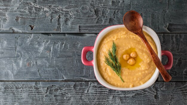 Vers gemaakte hummus in een paarse kom met een houten lepel op een donkere houten tafel