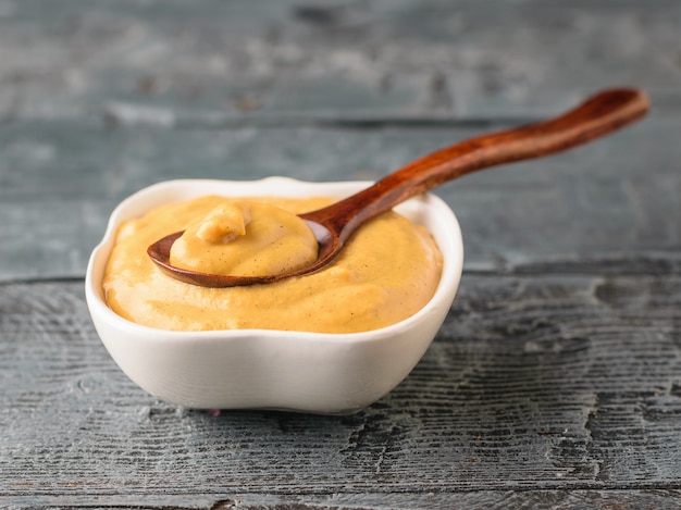 Vers gemaakte mosterdzaad saus in een witte kom op een rustieke tafel met een lepel