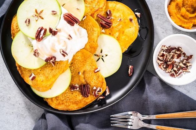 Vers gemaakte pompoenpannenkoekjes met groene appels op een zwarte serveerschaal