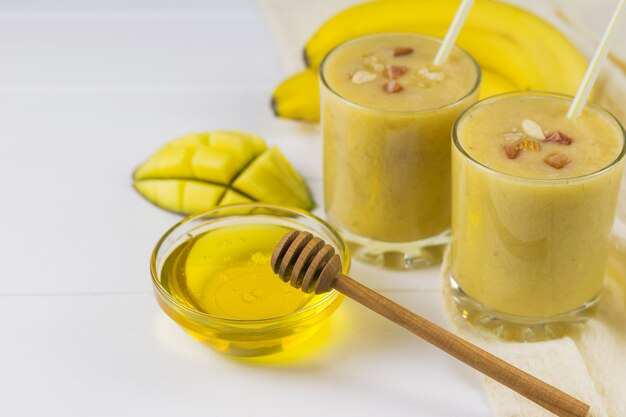 Vers gemaakte smoothies met mango, banaan, sinaasappel, honing en ontbijtgranen op een houten tafel