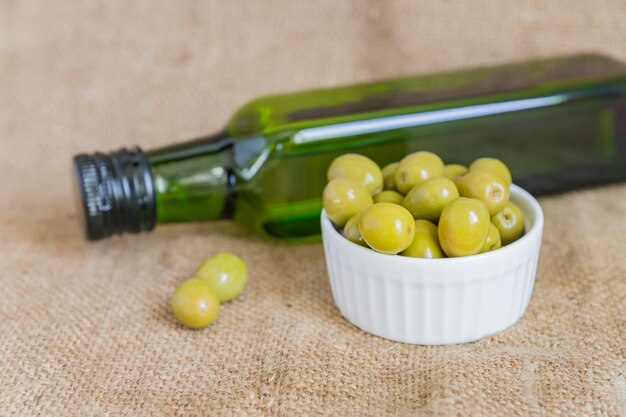 Foto vers gemarineerde groene olijven in witte keramische kom en groene fles premium olijfolie van eerste persing