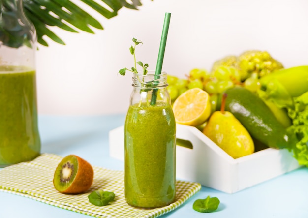 Vers gemengd groene smoothie in glazen flesje met groenten en fruit op het oppervlak. Gezondheid en detox-concept.