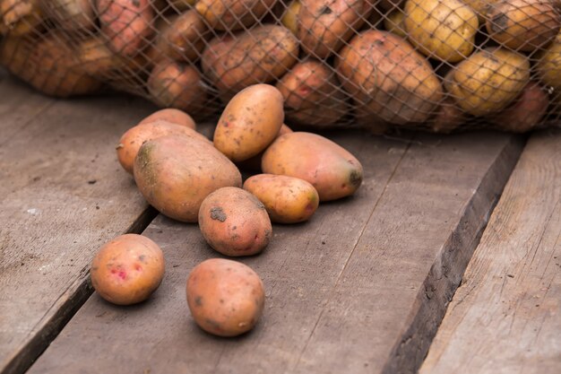 Vers geoogste aardappelen met grond nog op de huid, morsen uit een jute zak, op een ruw houten palet.