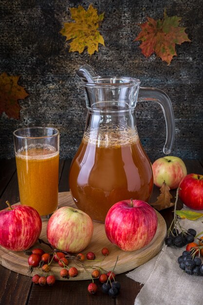 Vers geperst appelsap in een karaf en herfstbessen op een houten ondergrond.