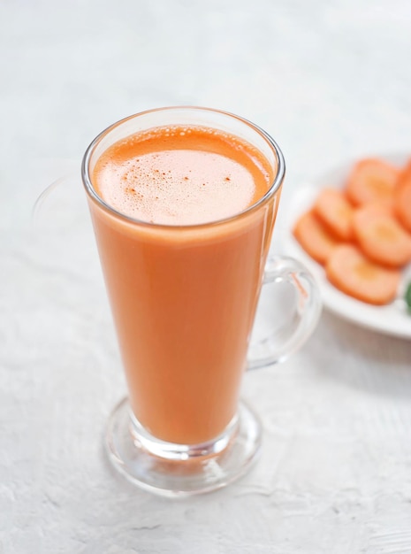 Vers geperst wortelsap staat in een glas op een betonnen tafel Achter is een bord gehakte wortelen Healthy food concept