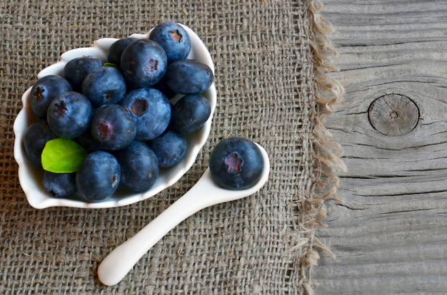 Vers geplukte biologische bosbessen in een witte kom op een jute doek. Bosbes. Bosbessen. Gezond eten, veganistisch eten of dieet concept met kopie ruimte. Selectieve aandacht.