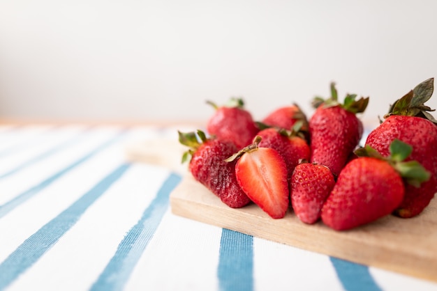 Vers gesneden aardbeien op een houten snijplank op een blauw en wit gestreept tafelkleed.