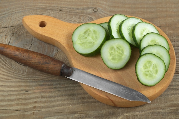 Vers gesneden komkommer en mes op houten snijplank