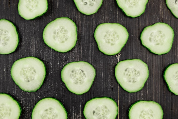 Foto vers gesneden komkommers op zwarte houten rustieke achtergrond, bovenaanzicht. plat lag patroon van groene komkommers op tafel, close-up