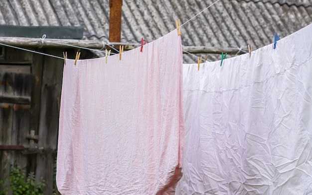 Vers gewassen beddengoed dat buiten aan het touw hangt. Kleren drogen in landelijke tuin.