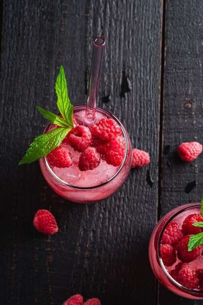 Vers ijs koud bessensap drankje met munt, zomer frambozen limonade in twee glazen met rietjes op donkere houten achtergrond, bovenaanzicht kopie ruimte