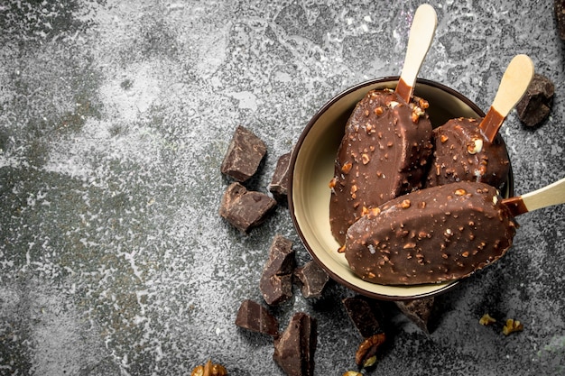 Vers ijs op een stokje in chocolade met noten. Op een rustieke achtergrond.