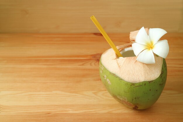 Vers jong kokosnotenwater in kokosnotenshell met Plumeria-bloem op houten lijst