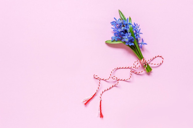 Vers mooi boeket van de eerste lente bosklokje kwik sneeuwklokjes bloemen met rood wit koord martisor traditioneel symbool van de eerste lentedag op roze achtergrond