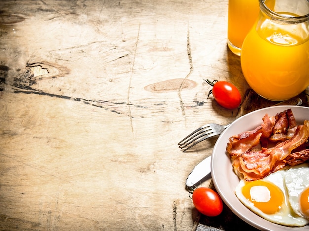 Vers ontbijt. jus d'orange met gebakken eieren, spek en sneetjes brood. op een houten tafel.